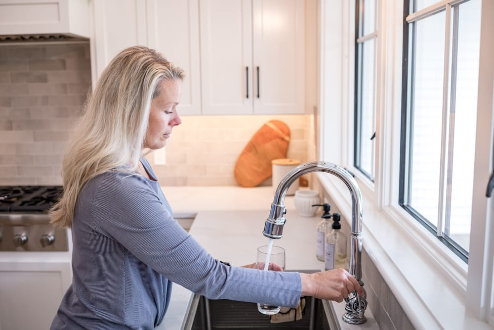 Client holding glass underneath water faucet.