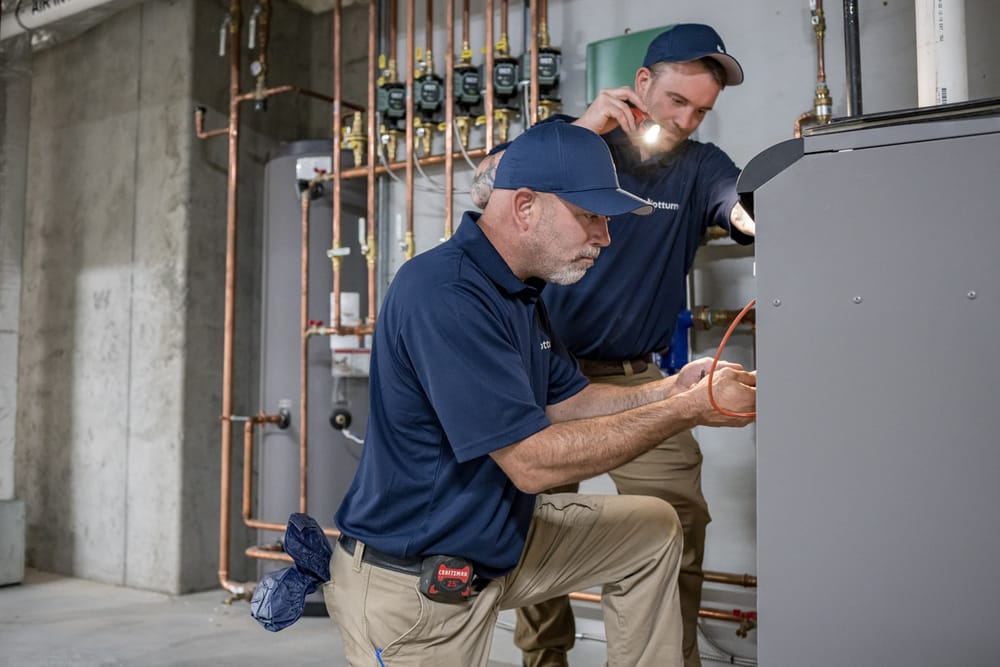 Two technicians kneeling in front of heater conducting heating services.