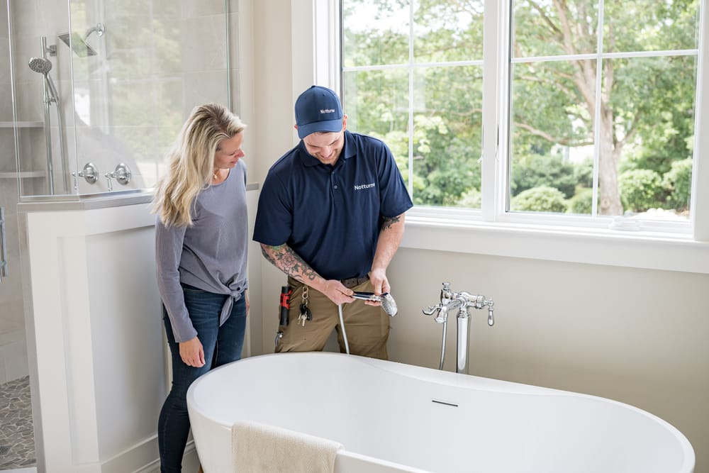 Plumber standing with client over a bathtub during a plumbing inspection.