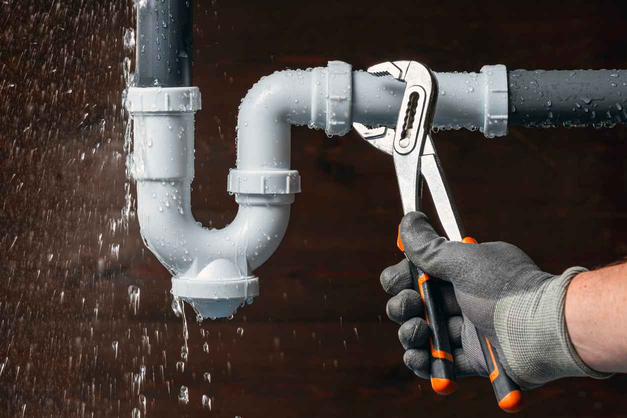 A plumber wearing a glove fixing a leaky pipe with a wrench