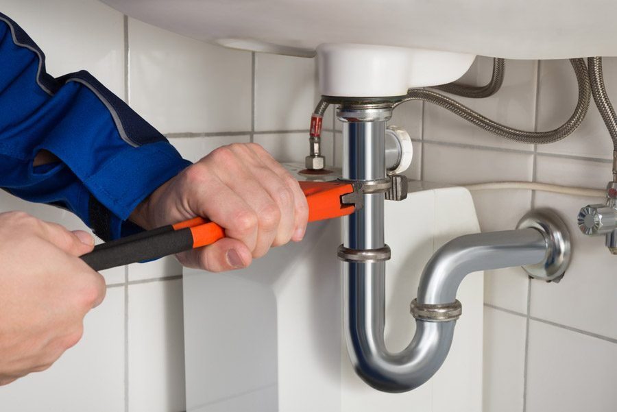 Plumber using a wrench to repair a pipe under a bathroom faucet