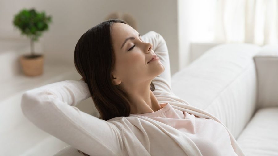 Woman lounging on a white sofa with eyes closed, looking relaxed and content.