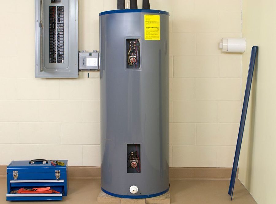 A water heater in the basement of a home with electrical panel mounted on wall next to it