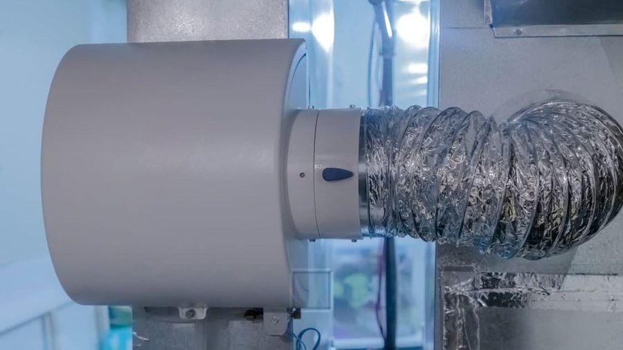 Close-up of a flexible spiral aluminum duct connected to a beige industrial housing in a lab or workshop setting